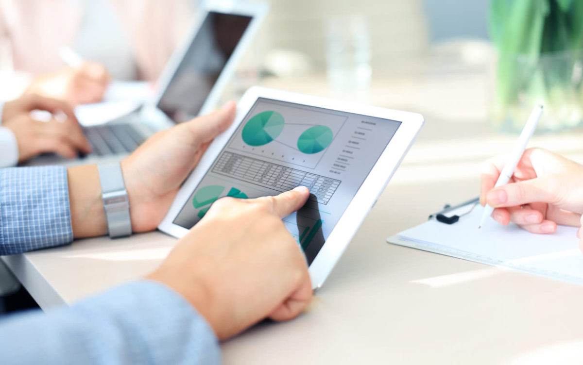 a person using a tablet to show data and charts while other employees take notes