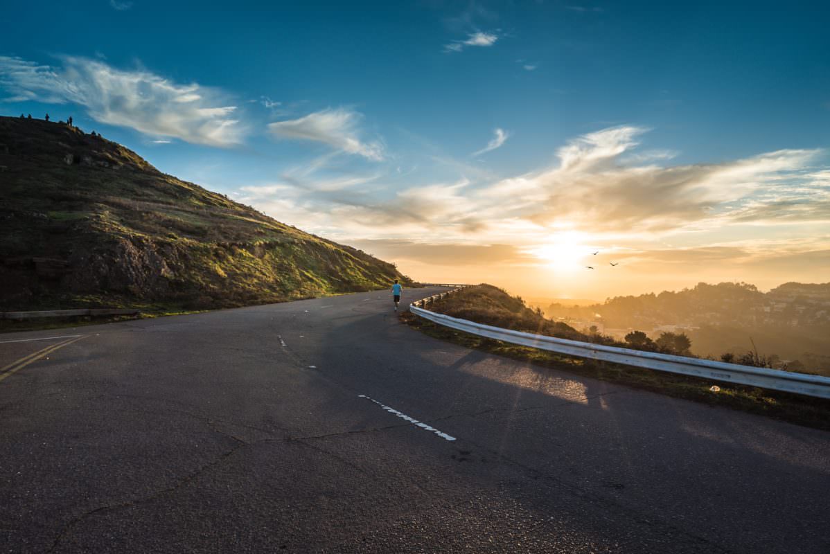 highway on a mountain overlooking a sunset and a person jogging in the distance