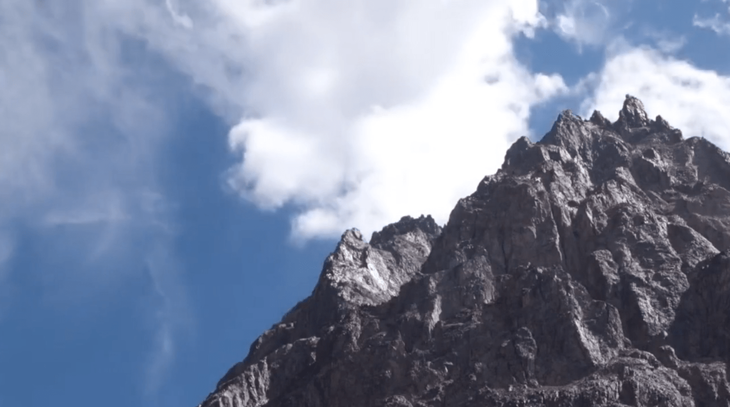 A rocky mountain peek with clouds and a blue sky above it