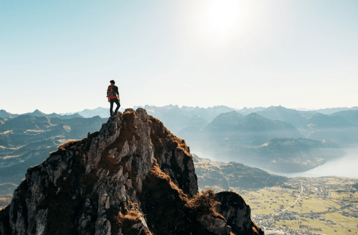 A hiker atop a mountain looking out at other mountains and lakes